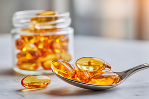 Close-up view of soft gel capsules in a spoon with jar in background, a Health & Medical Photo by AlyaAnd