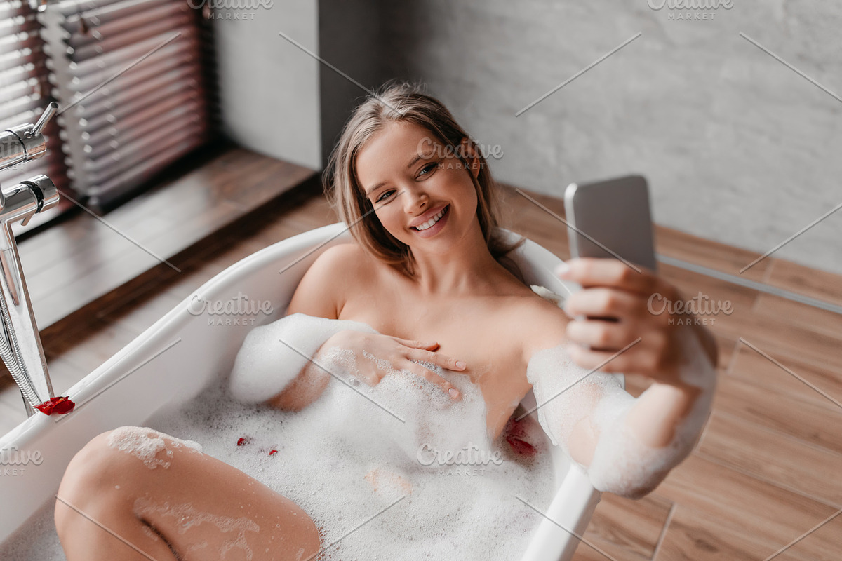 Pretty lady relaxing in foamy bath and taking selfie on smartphone while enjoyi, a Photo by Prostock-Studio (Photo 2 of 2)