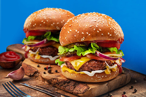 Tasty cheeseburgers on wooden tray close-up. Blue background., a Food & Drink Photo by Volff