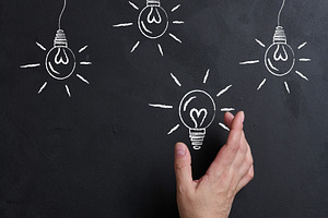 A hand reaches out to a chalk-drawn glowing light bulb on a blac, a Business Photo by ndanko