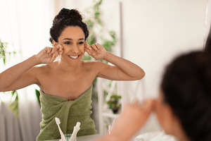 Lovely young woman making lymphatic drainage facial self massage near mirror at, a Photo by Prostock-Studio