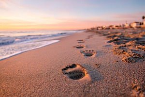 Footprints in light sand lead along a tranquil beach at sunset, a Photo by AlyaAnd