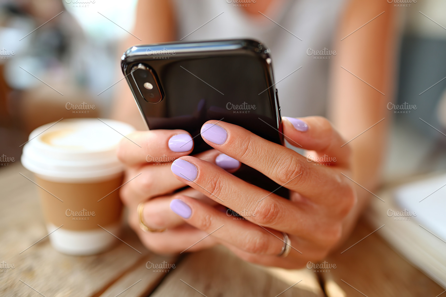 Female hand holding smartphone with lavender nails at outdoor cafe table, a Photo by AlyaAnd