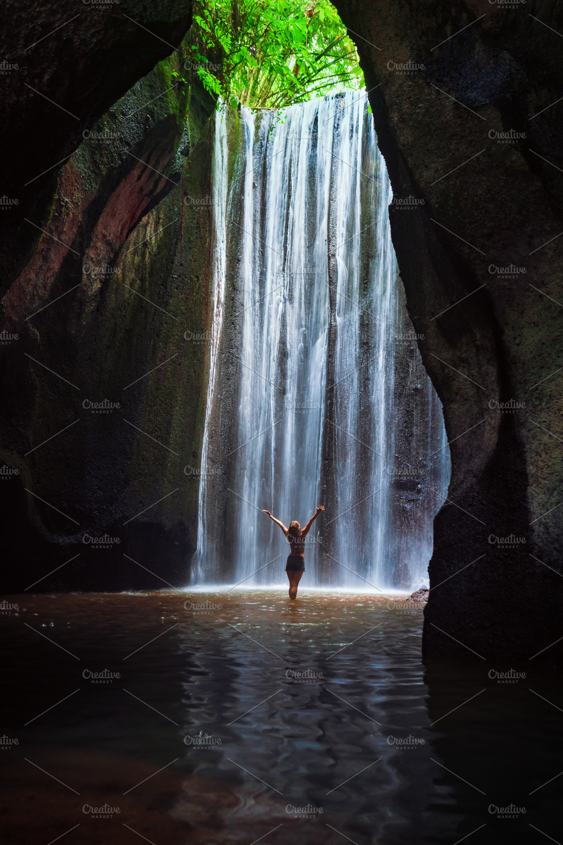 Woman stand under cave waterfall featuring bali, travel, and indonesia, a Person Photo by Tropical Studio