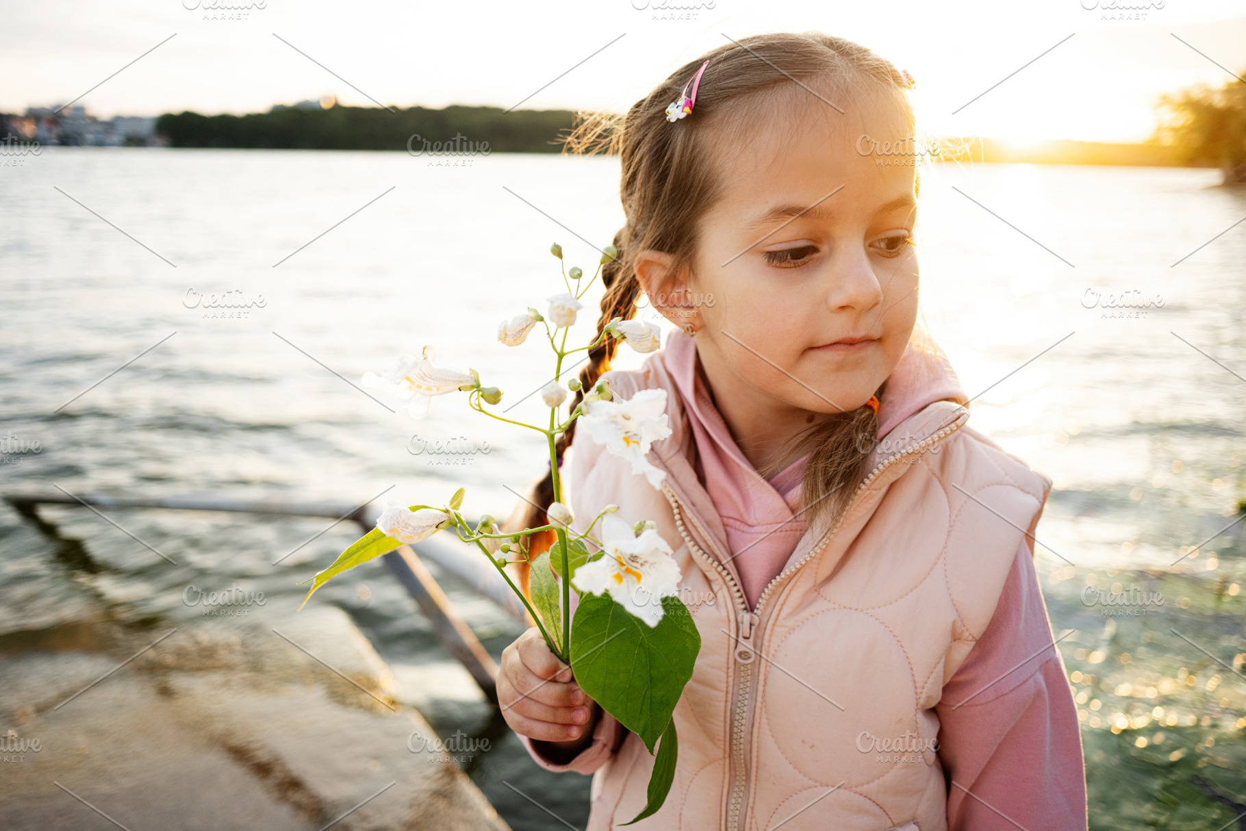 Young girl holding flowers by a lake during a peaceful sunset moment, a Photo by AS photostudio