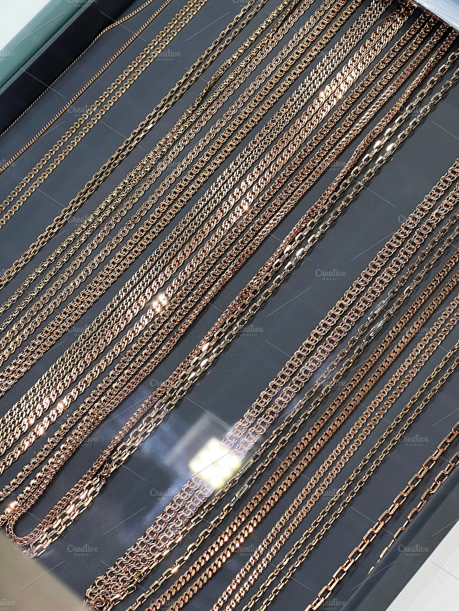 Closeup of multiple gold and rose gold chains displayed in a jewelry showcase, a Photo by AS photostudio