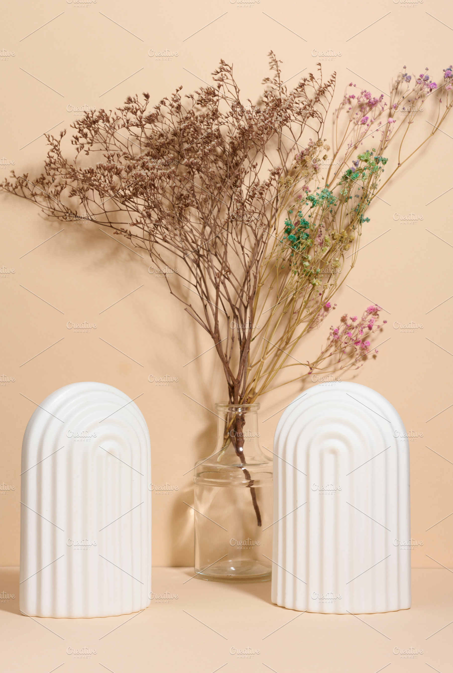 A vase with dried flowers and two white fluted arches on a beige, a Background Photo by ndanko