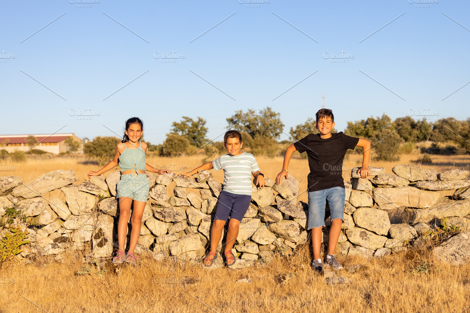 Three kids in front of a stone wall at summer, a Person Photo by Cosca
