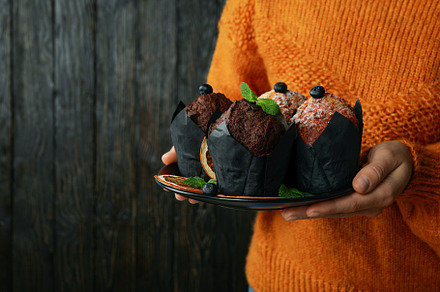 Woman in sweater holds plate with muffins, space for text, a Food & Drink Photo by AtlasStudio PRO