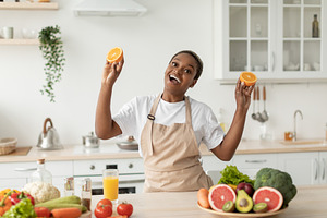Glad emotional young black woman in apron have fun on minimalist kitchen interi, a Person Photo by Prostock-Studio