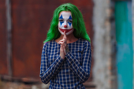 Portrait of a greenhaired girl in chekered dress with joker makeup on a rusty m