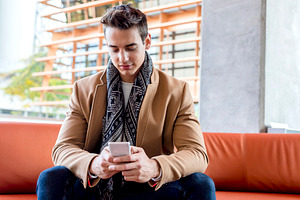 Smiling young man using phone on modern leather sofa, a Person Photo by RF Images