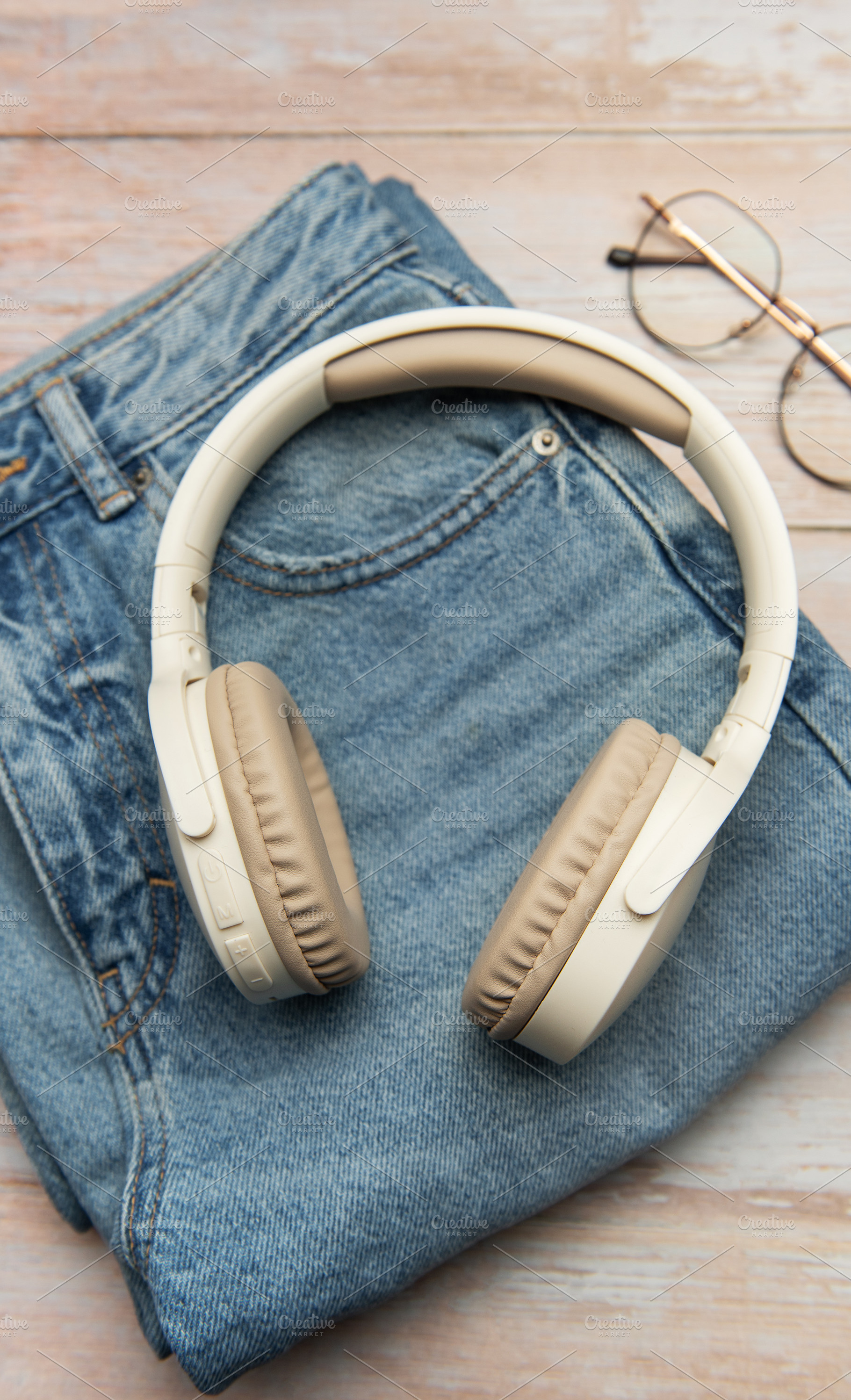 Wireless headphones lying on folded jeans and eyeglasses on wood, a Business Photo by Olena Rudo