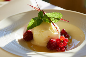 Creamy vanilla ice cream scoop topped with fresh red berries and mint, drizzled, a Photo by Studio ANNA