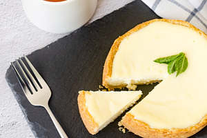 Classic cheesecake with mint leaf and cup of tea on black slate, a Food & Drink Photo by vimart