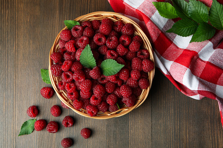 Raspberries in a wicker bowl and a tea towel on a wooden table, a Food & Drink Photo by AtlasStudio