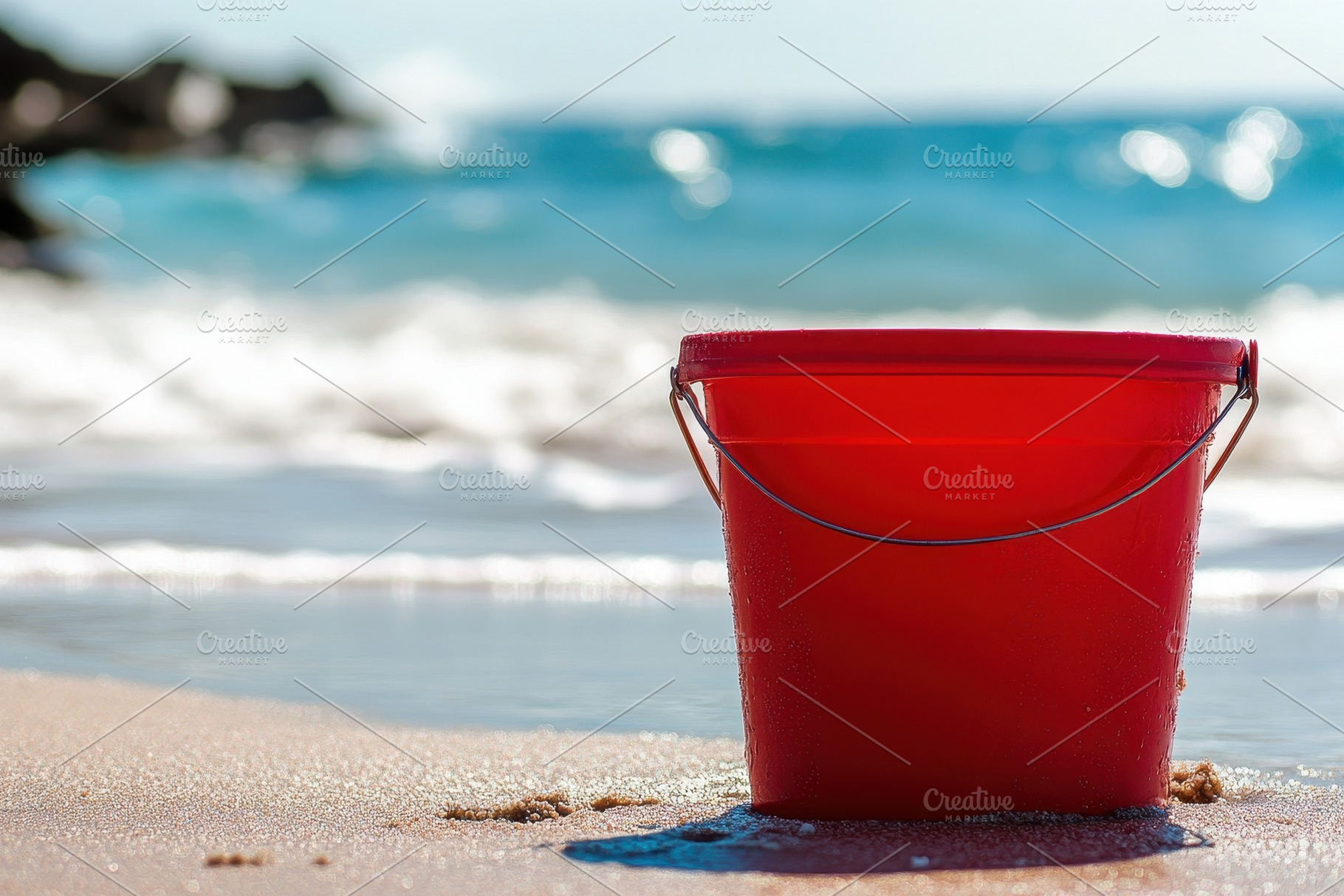 Vibrant red bucket rests on sandy, a Photo by Pavel_design