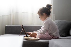 Little girl using tablet on sofa at home, child screen time and digital lifesty, a Food & Drink Photo by etorres69