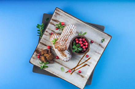 Cream eclairs choux pastries served with fresh cranberries on a