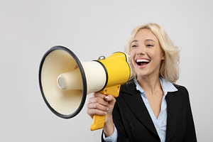 Positive female entrepreneur shouting into megaphone on light grey studio backg, a Photo by Prostock-Studio