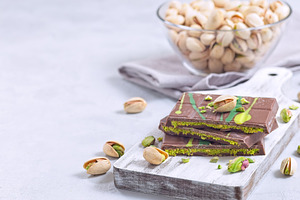 Milk chocolate bar with pistachio and kadaifi filing, lying on cutting board, h, a Food & Drink Photo by iuliia_n