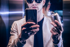 Man on an elevator taking a selfie and holding a metallic soda c, a Person Photo by DanFLCreativo