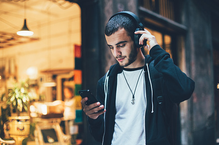 Young man with headphones uses phone containing man, music, and background, a Technology Photo by DeRepente