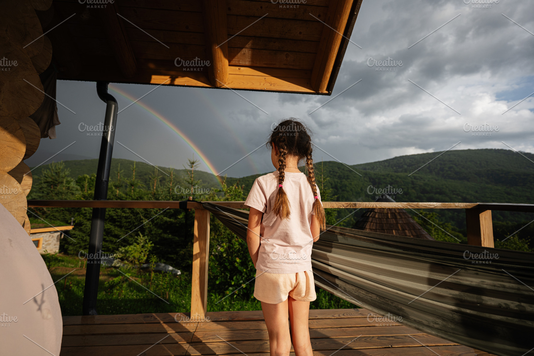 Girl standing on balcony with rainbow and mountain view in the background, a Photo by AS photostudio