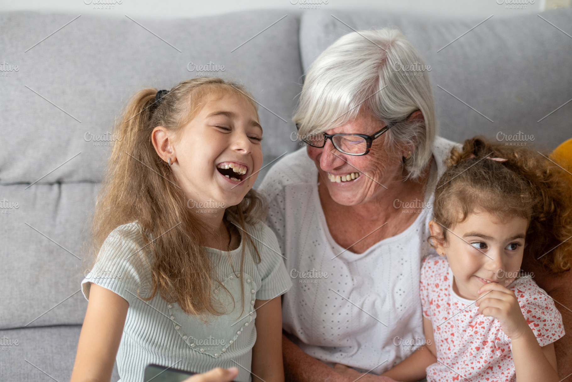 Grandmother laughing with granddaughters on sofa at home, a Person Photo by etorres69