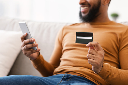Black Man Holding Credit Card Using Phone Sitting At Home, a Background Photo by Prostock-Studio