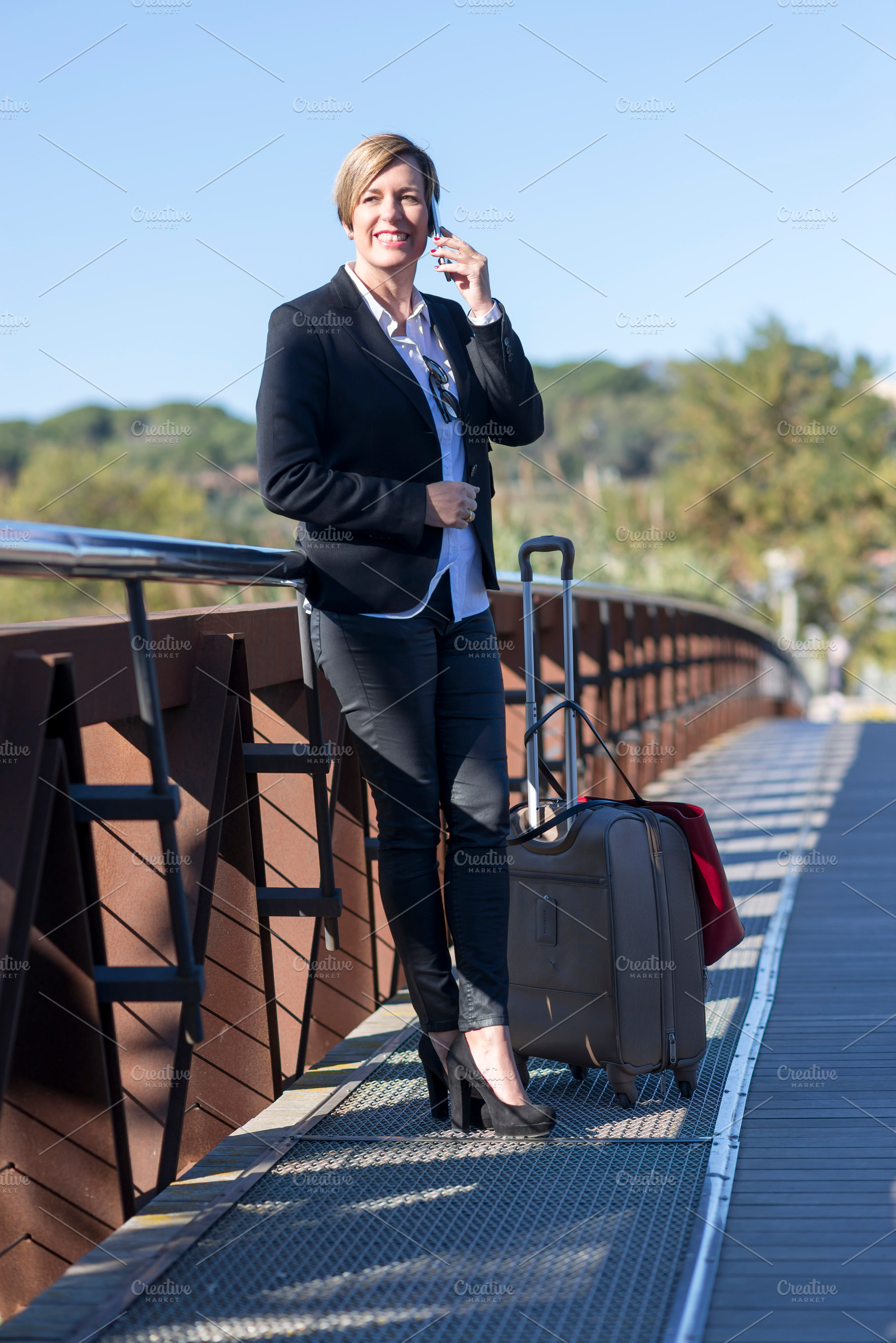 Businesswoman with suitcase walking on city bridge, a Photo by RF Images