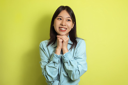 Cheerful Asian Female Posing Holding Hands Near Face, Yellow Background, a Person Photo by Prostock-Studio
