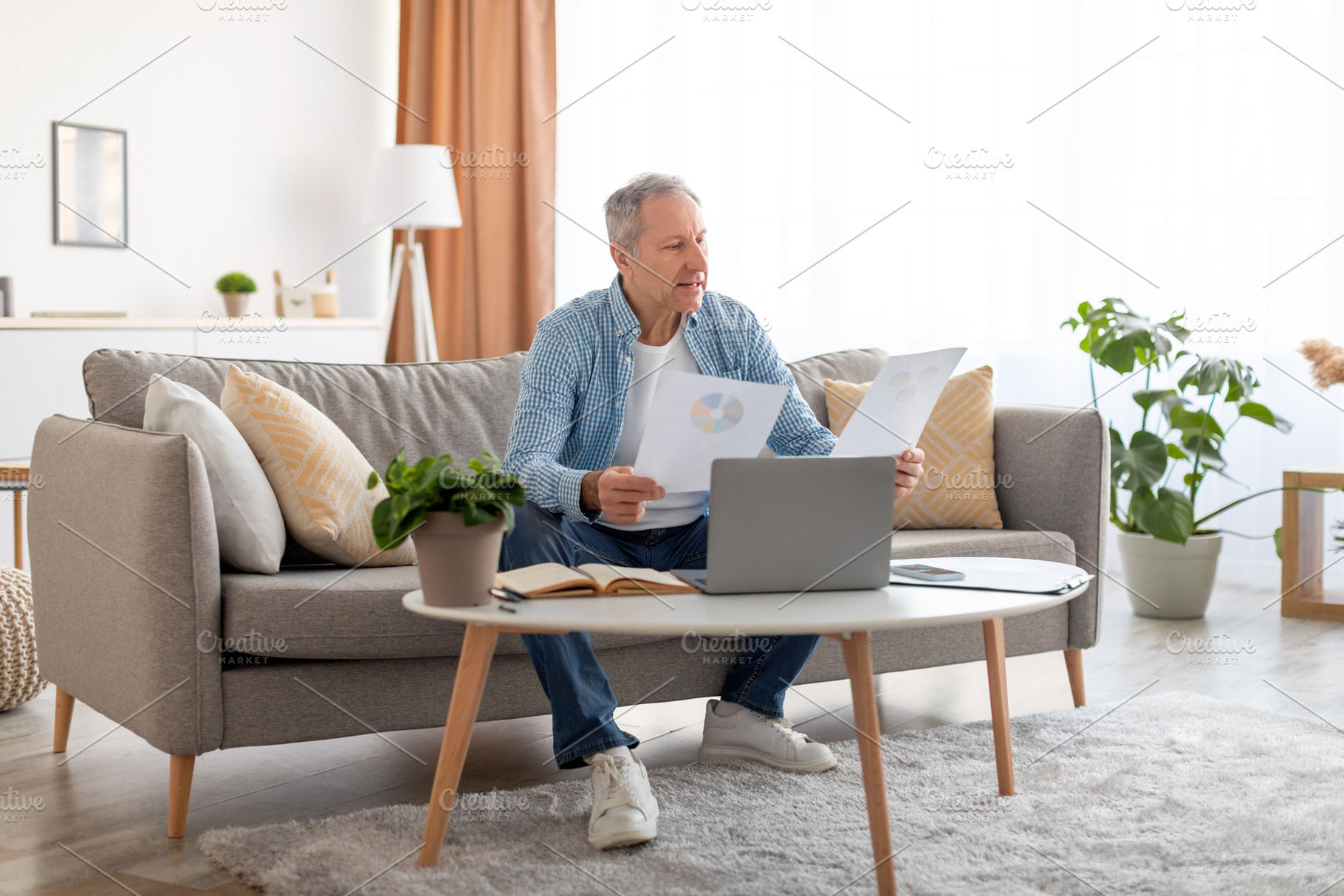 Man holding documents reading report working on laptop at home, a Photo by Prostock-Studio