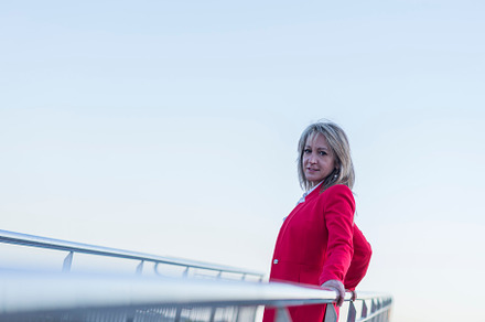 Adult woman wearing red jacket relaxing while leaning on railing outdoors, a Person Photo by 2Design