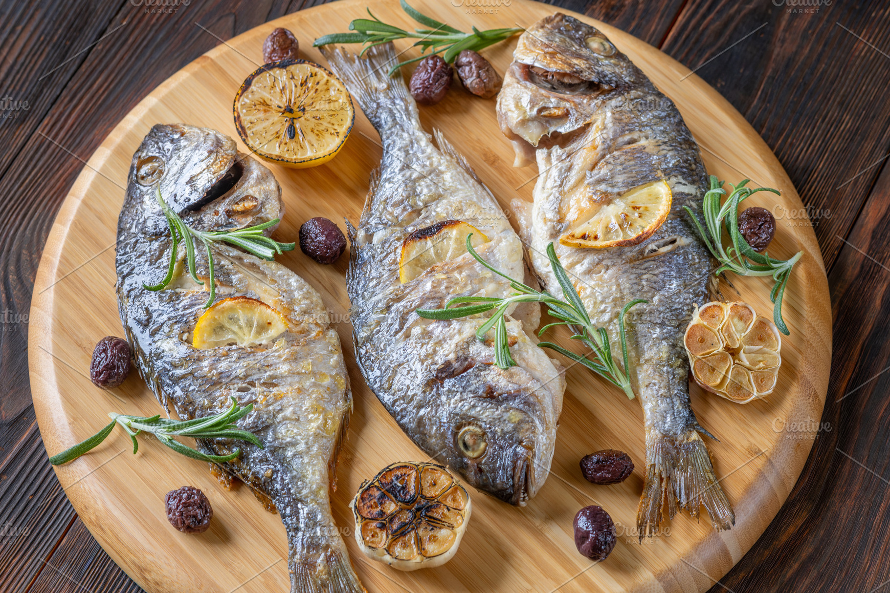Three roasted sea bream with lemon rosemary olives and garlic on, a Food & Drink Photo by Alexander Prokopenko