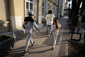 Family walks together along a sunny city sidewalk by residential buildings, a Person Photo by AS photostudio