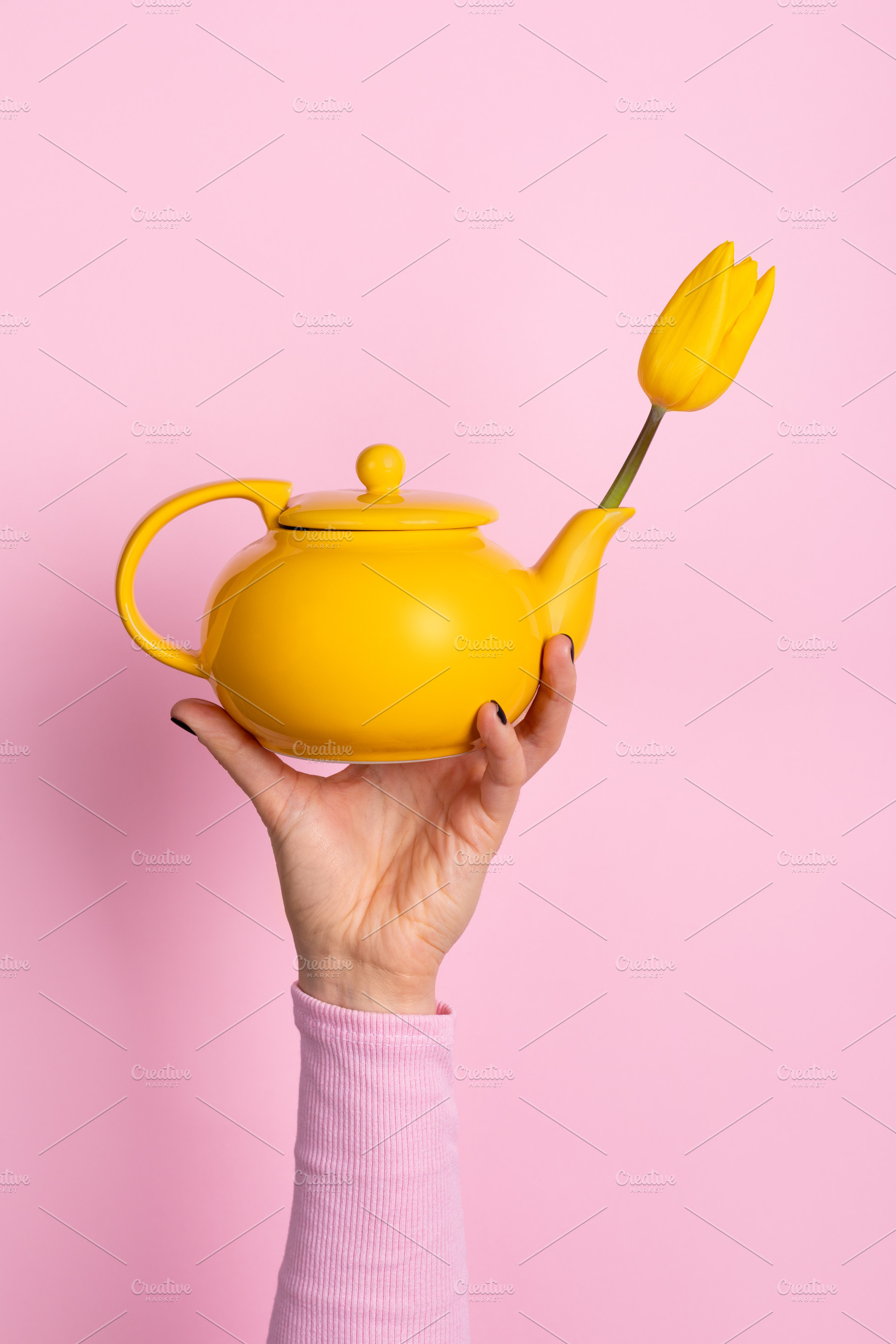 Hand holding a bright yellow teapot with a yellow tulip on a pas, a Holiday Photo by Ales Munt