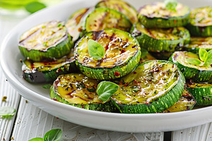 Grilled zucchini pieces in plate on wooden table, a Food & Drink Photo by AlyaAnd