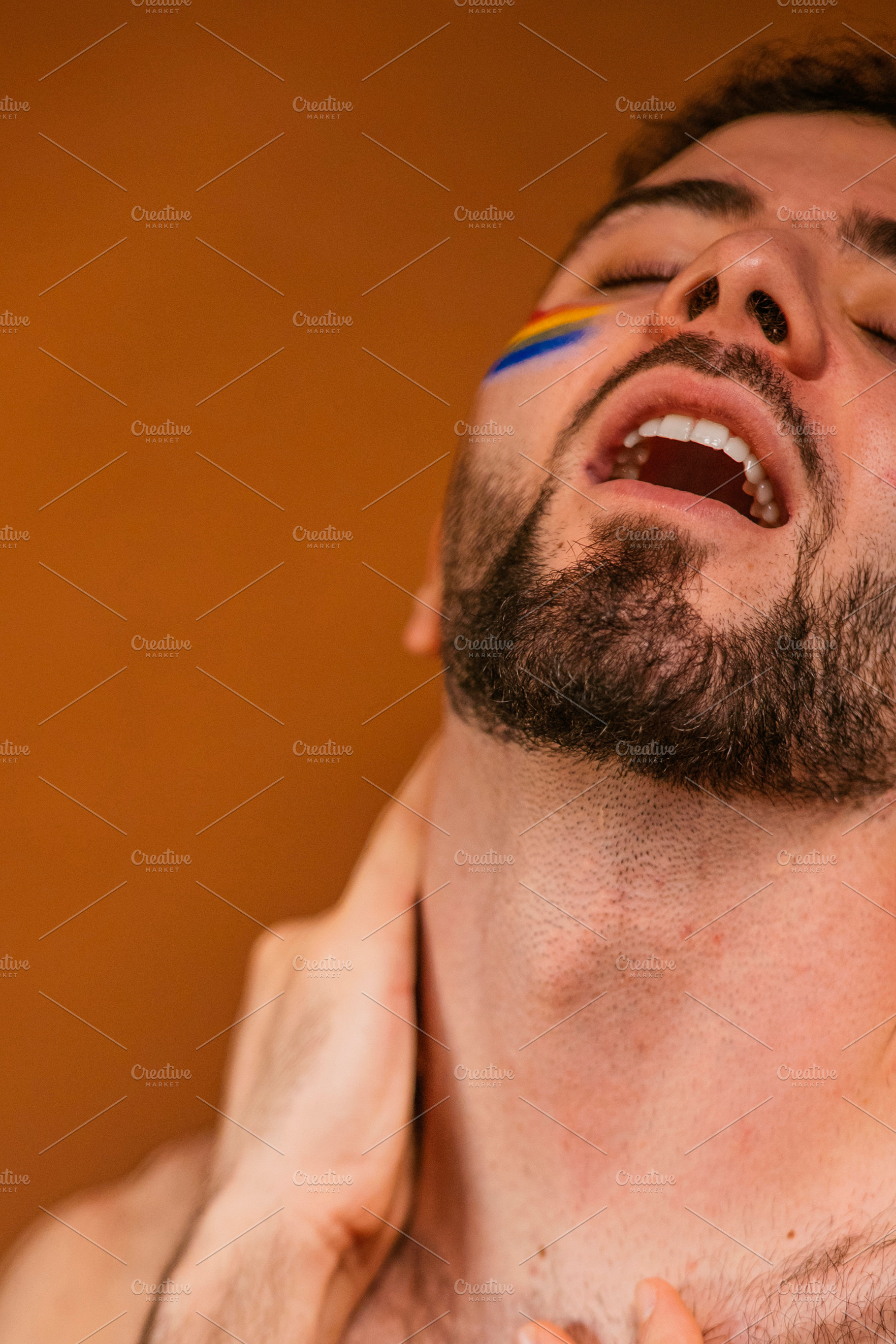 Man with rainbow face paint experiencing joy and freedom, a Photo by karrastock