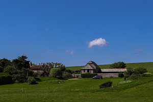 Rural landscape with a traditional stone barn, green grass fields, and blue sky, a Photo by Studio ANNA