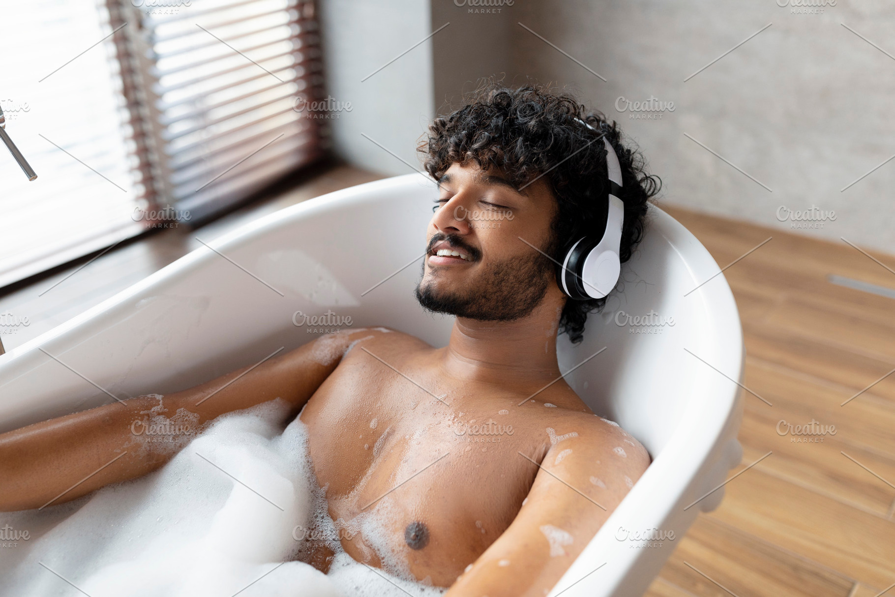 Relaxed indian man listening to calming music in wireless headphones, lying in, a Person Photo by Prostock-Studio
