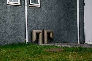 Metallic ventilation pipes outside a grey building in Akranes, surrounded by gr, a Photo by AS photostudio
