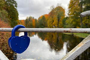 A blue heart-shaped padlock on a metal railing by a river with autumn trees., an Industrial Photo by Textures & Backgrounds