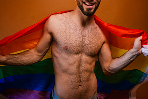 Young adult man smiling at camera holding a rainbow flag, a Photo by karrastock