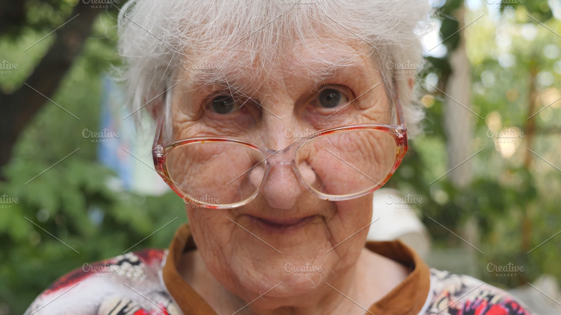 Old woman in eyeglasses looking into camera and smiling outdoor. Portrait of happy granny in glasses spending time outside. Emotions of grandmother. Close up Slow motion, a Person Photo by Footage Autor