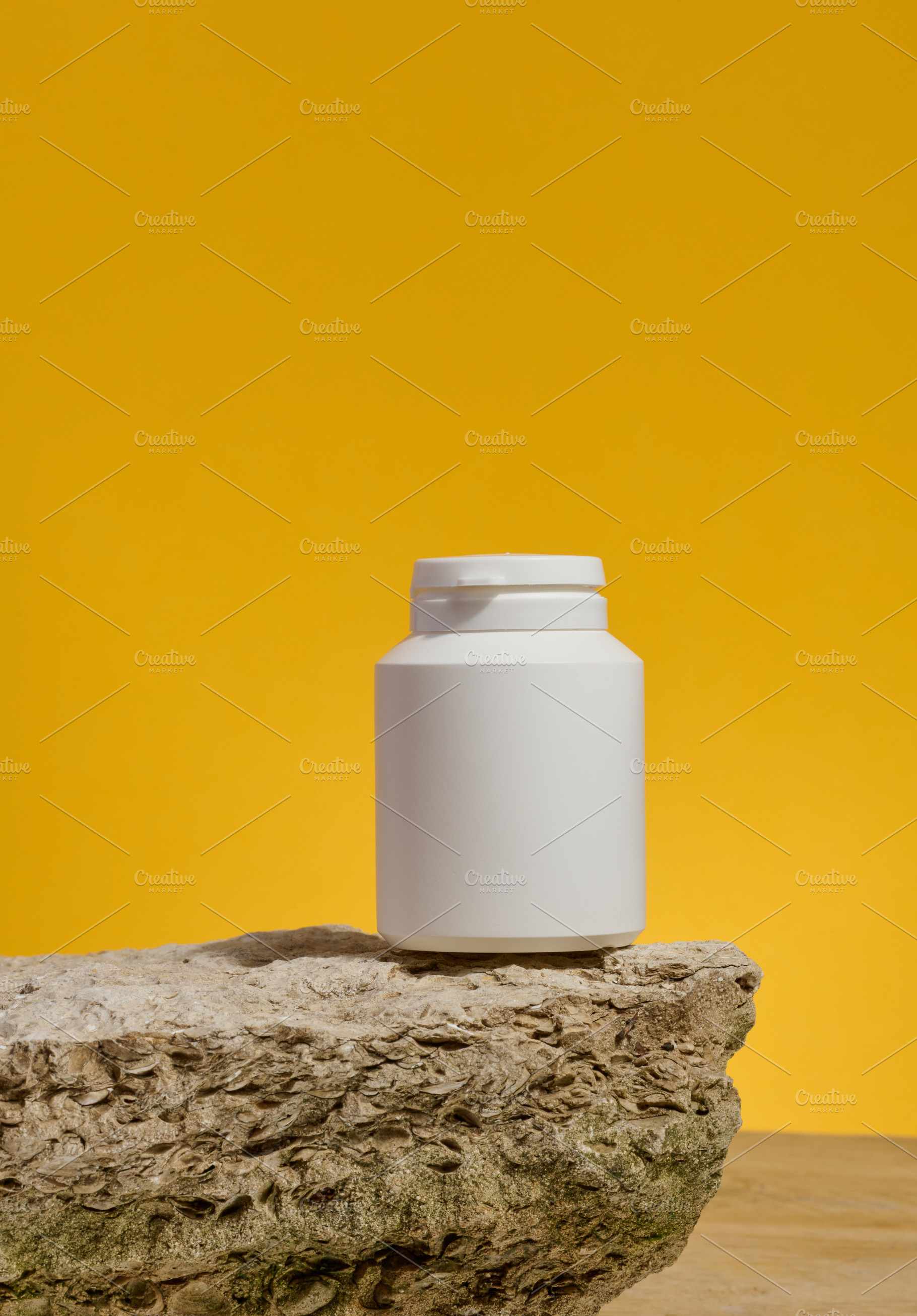 White plastic medicine jar on stone, yellow background. Mock up, a Health & Medical Photo by ndanko