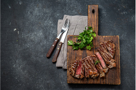 Fried strip loin steak on wooden, a Food & Drink Photo by LARISA BLINOVA