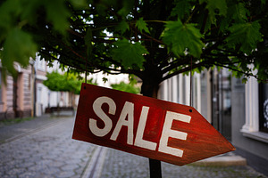Red sale sign hanging on tree branch in urban street setting, a Photo by AS photostudio
