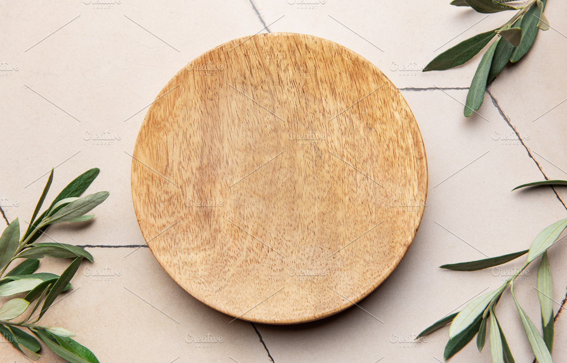 Empty round wooden plate with olive branches on tiled surface, a Background Photo by Olena Rudo
