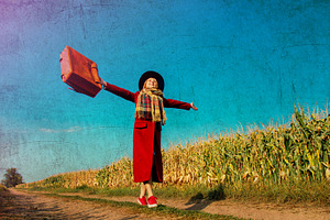 girl coat with suitcase on a rural road near cornfield